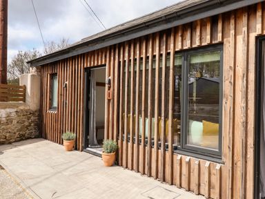 The exterior of a wooden building with windows door and two potted plants on the pavement outside at 1 Caddaford Barns Buckfastleigh