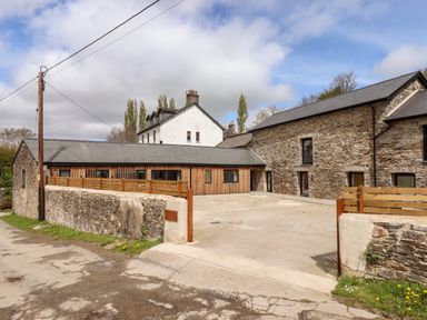 Stone and wood buildings with a paved courtyard and a wooden fence at 1 Caddaford Barns in Buckfastleigh