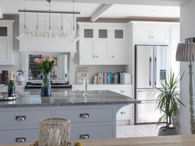 A kitchen with white cabinets a stainless steel refrigerator a marble countertop an island with flowers on it and a potted plant at Trewartha in Praa Sands