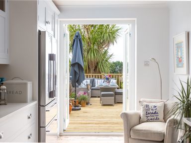 A kitchen area leading to a wooden deck with outdoor seating and plants at Trewartha in Praa Sands