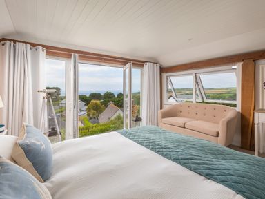 A bedroom with a bed pillows sofa telescope open windows and a view of houses and countryside at Trewartha in Praa Sands