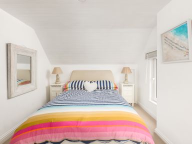 A bedroom with a double bed striped bedspread bedside tables lamps a mirror and a beach picture on the wall at Trewartha in Praa Sands
