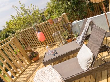 An outdoor wooden deck with two lounge chairs a blanket and plants on the railing at Trewartha in Praa Sands