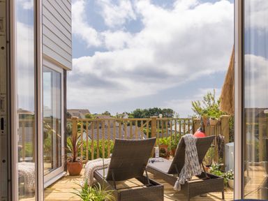 A balcony with two lounge chairs and potted plants overlooking rooftops at Trewartha in Praa Sands