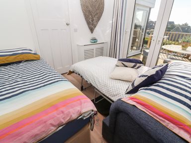 A bedroom with two single beds and a foldout bed near glass doors opening to a deck with a table and chairs at Trewartha in Praa Sands