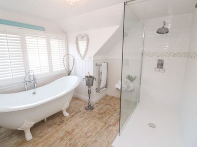 A bathroom with a clawfoot bathtub next to a window with shutters and a walk-in shower at Trewartha in Praa Sands