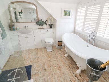 A bathroom with a white clawfoot bathtub a toilet a sink with a mirror above and wooden floor at Trewartha in Praa Sands