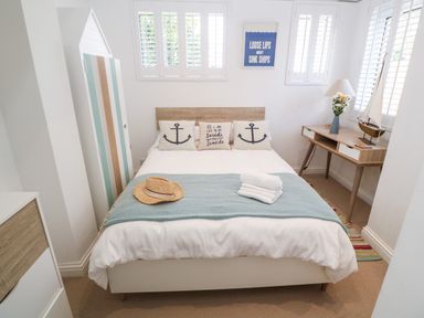 A bedroom with a bed and nautical themed pillows a wooden desk with a model sailboat and flowers at Trewartha in Praa Sands