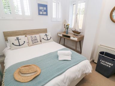 A bedroom with a bed with anchor pillows a nightstand with a lamp and model boat and a laundry basket at Trewartha in Praa Sands