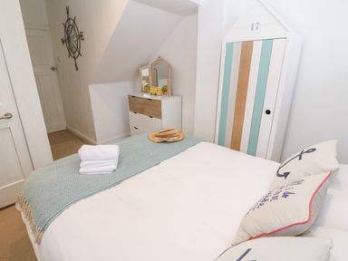 A bedroom with a bed folded towels a hat a chest of drawers a mirror and a striped cabinet at Trewartha in Praa Sands