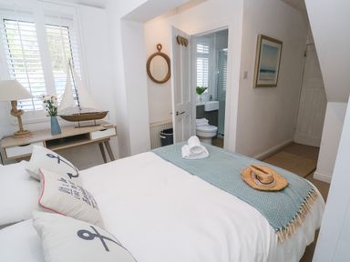 A bedroom with a bed a desk with a lamp and model sailboat and an open door leading to a bathroom at Trewartha in Praa Sands