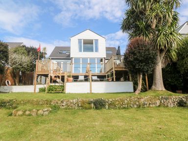 A two-story house with a wooden deck overlooking a grassy lawn with trees and stone edging at Trewartha in Praa Sands