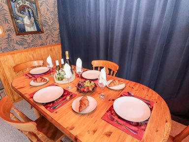 A dining table with plates croissants a fruit bowl and bottles in a room with wooden chairs and patterned wallpaper at Tartaria in Widdrington