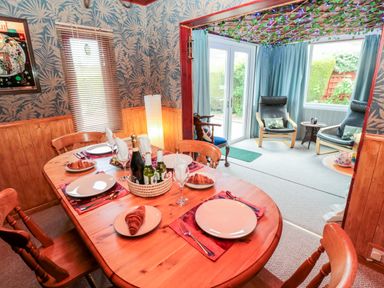 A dining room with a wooden table set with plates croissants and bottles next to a sunroom with armchairs and a window at Tartaria in Widdrington