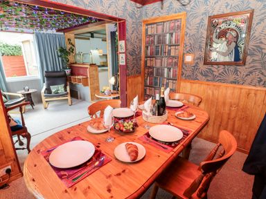 A dining room with a wooden table set with plates croissants and glasses next to a sitting area with chairs and plants at Tartaria in Widdrington