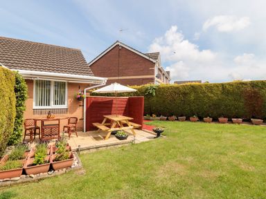 A backyard with a patio table and chairs an umbrella and potted plants at Tartaria in Widdrington