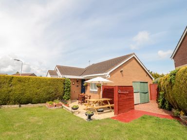 A backyard with a picnic table umbrella garden furniture and storage sheds at Tartaria in Widdrington