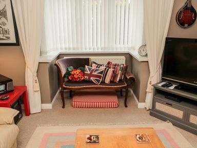 A living room corner with a small vintage sofa with cushions and a striped pet bed underneath at Tartaria in Widdrington