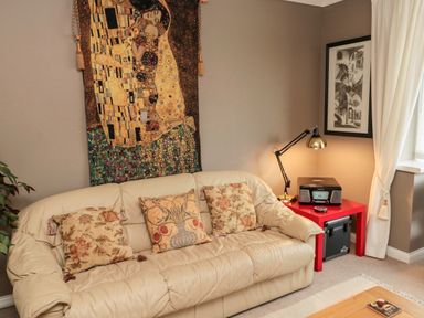 A beige leather sofa with three patterned cushions and a tapestry above it in a living room at Tartaria in Widdrington