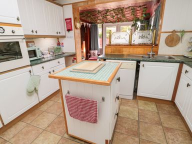 A kitchen with white cabinets green countertops an island with a chopping board and checked towel and an oven toaster and microwave at Tartaria in Widdrington