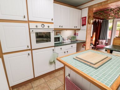 A kitchen with white cabinets a built-in oven a green toaster and microwave a tiled counter with chopping boards and a view of a seating area with a pink chair at Tartaria in Widdrington