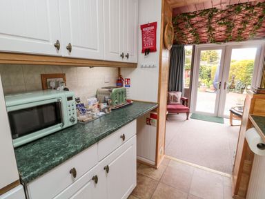 A kitchen counter with a microwave toaster and condiments next to a room with chairs and glass doors leading outside at Tartaria in Widdrington