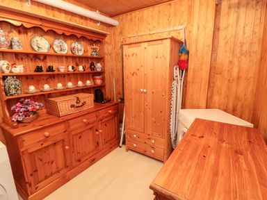 A wooden paneled room with wooden cabinets shelves teacups plates an ironing board and a washing machine at Tartaria in Widdrington