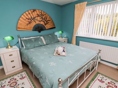 A bedroom with a double bed green bedspread two white bedside tables with green lamps and a large fan decoration on the wall at Tartaria in Widdrington