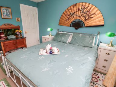A bedroom with a bed with green floral bedding and a large decorative fan on the wall at Tartaria in Widdrington