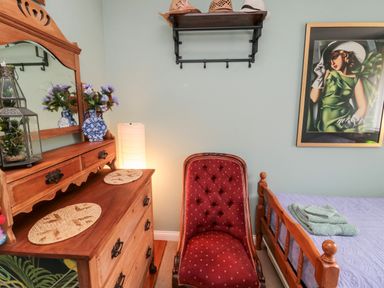 A bedroom with a wooden dresser and mirror a red upholstered chair a bed with folded towels and a framed painting at Tartaria in Widdrington