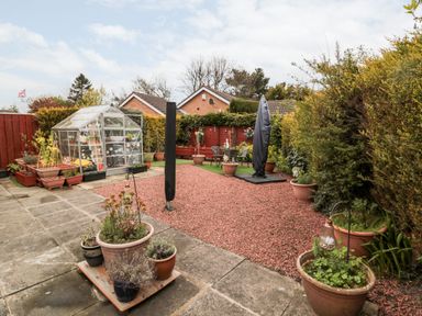 A backyard garden with a small greenhouse multiple potted plants and covered patio furniture at Tartaria in Widdrington