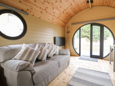 An interior room with a gray sofa and striped cushions near a large circular window and door at Willow Pod in Arundel West Sussex