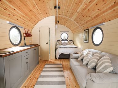 A wooden pod interior with a kitchen area on the left a bed in the back and a sofa with striped cushions on the right at Willow Pod in Arundel West Sussex