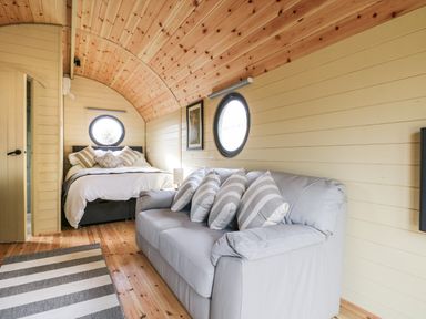 A bedroom with a bed and a sofa with striped cushions and round windows at Willow Pod in Arundel West Sussex