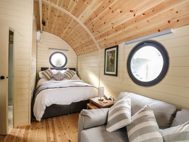 A bedroom with a bed pillows sofa table lamp and two round windows at Willow Pod in Arundel West Sussex