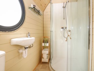 A bathroom with a round window a wall-mounted sink a glass shower enclosure and a small shelf with a plant at Willow Pod in Arundel West Sussex