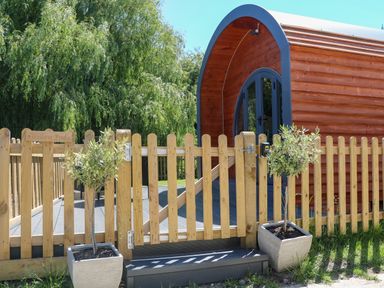A wooden fence and gate with potted plants outside a curved wooden pod structure at Willow Pod in Arundel West Sussex