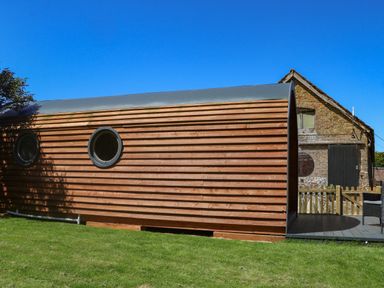 A wooden pod with circular windows next to a brick building on a grassy lawn at Willow Pod in Arundel West Sussex