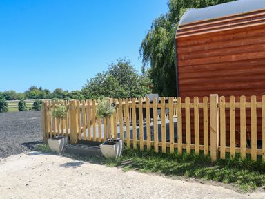A wooden fenced area with two potted plants and outdoor seating beside a wooden structure at Willow Pod in Arundel West Sussex