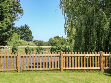 A garden with a wooden fence and green trees in the background at Willow Pod in Arundel West Sussex