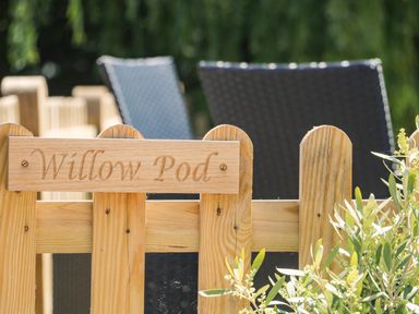 A wooden fence with a carved sign reading Willow Pod and outdoor chairs in the background at Willow Pod in Arundel West Sussex