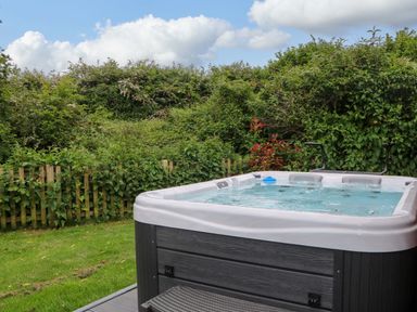 An outdoor hot tub on a deck next to a green garden with a wooden fence at Willow Pod in Arundel West Sussex