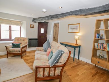 A sitting room with a floral sofa and armchair next to a window a wooden bookshelf and a small table with a lamp at Ashness in Bassenthwaite near Keswick