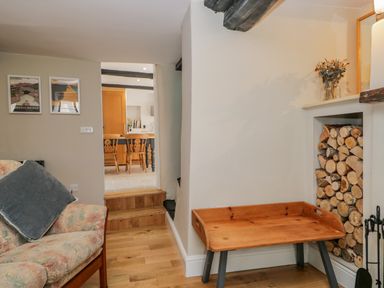 A sitting area with a floral armchair a wooden tray table and stacked firewood near a fireplace at Ashness in Bassenthwaite near Keswick