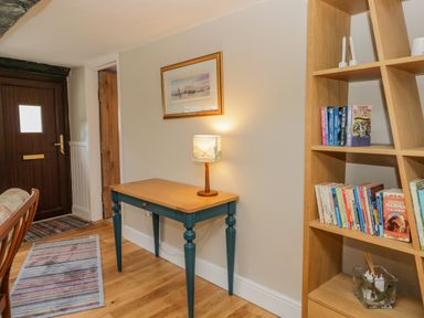 A hallway with a wooden door a small table with a lamp a framed picture on the wall and a wooden bookshelf with books and candles at Ashness in Bassenthwaite near Keswick