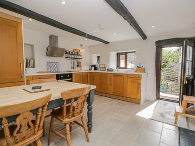 A kitchen with wooden cabinets a dining table with chairs and an open door leading outside at Ashness in Bassenthwaite near Keswick