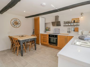 A kitchen with wooden cabinets a dining table with four chairs and kitchen utensils on shelves at Ashness in Bassenthwaite near Keswick