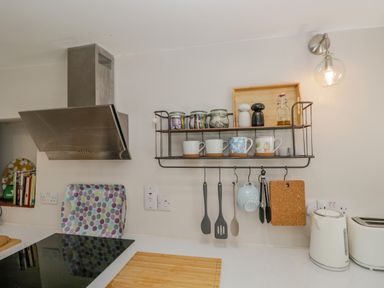 A kitchen with a stove hood cups and jars on a metal shelf and utensils hanging below with a kettle and toaster on the counter at Ashness Bassenthwaite near Keswick