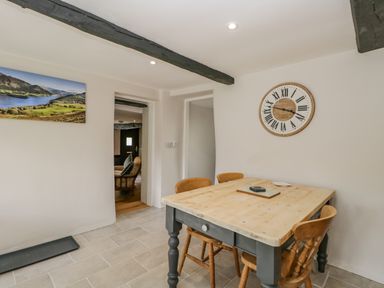 A dining area with a wooden table and four chairs a large wall clock and a landscape picture at Ashness Bassenthwaite near Keswick