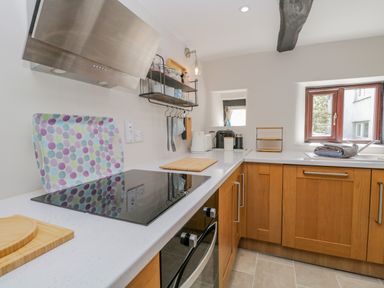 A kitchen with wooden cabinets a stovetop a kettle and a window at Ashness in Bassenthwaite near Keswick